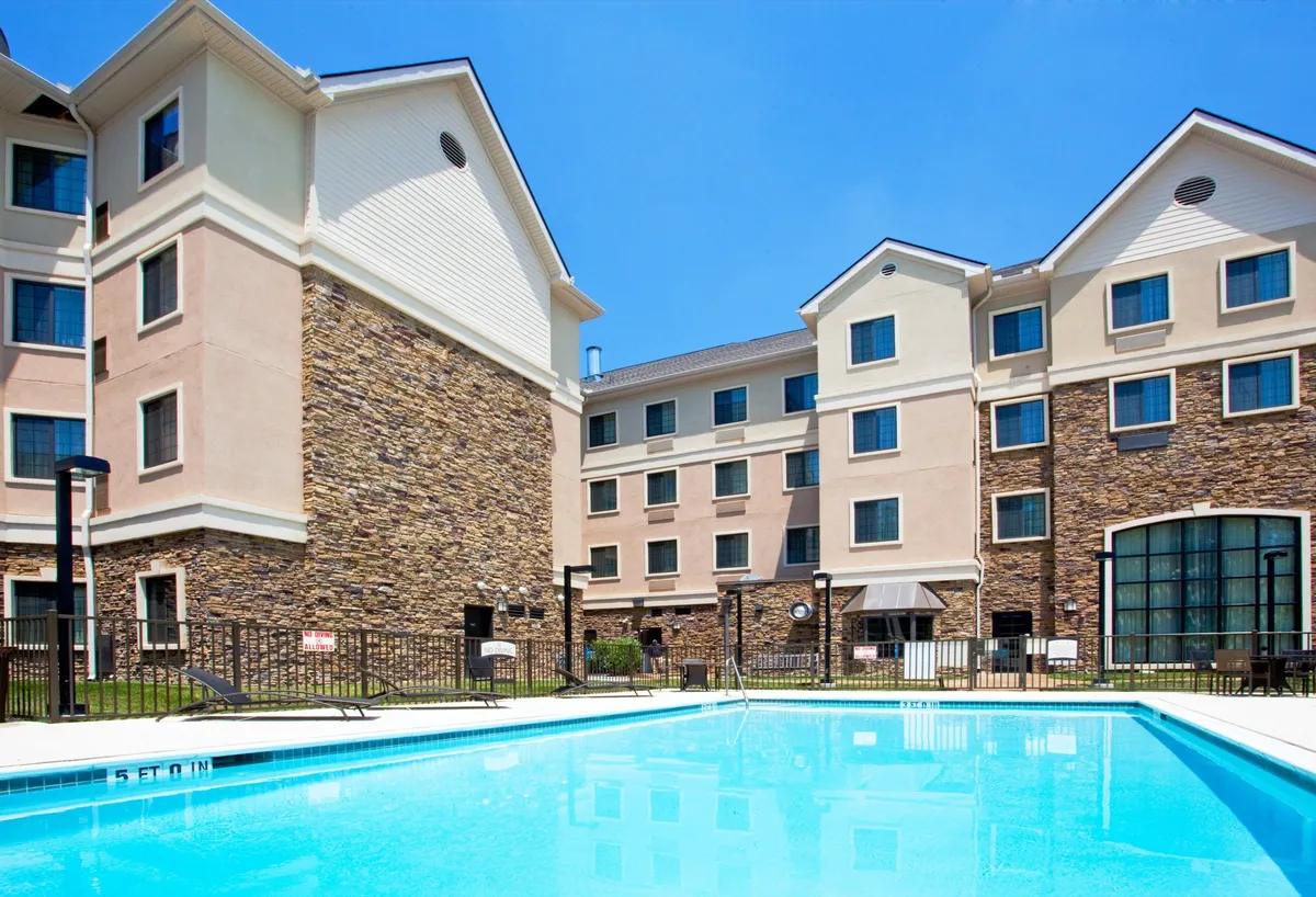 This image captures a sparkling outdoor swimming pool adjacent to the hotel building, with several lounge chairs and an outdoor seating area where guests can relax, sunbathe, or socialize. The scene is bathed in natural sunlight, evoking the vibrant atmosphere of summer afternoons and casual poolside gatherings.