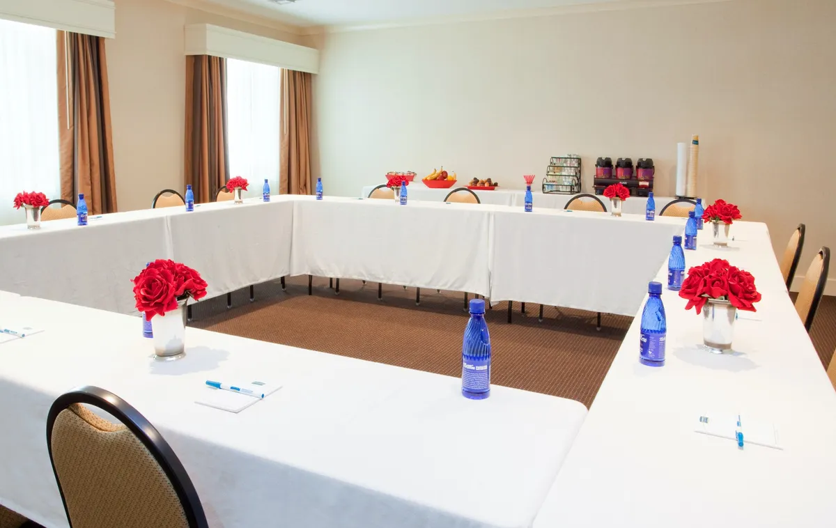 The image shows a long conference table set for meetings or workshops, decorated with red floral arrangements, blue water bottles, and a variety of snacks. The mood is collaborative and focused, ideal for team brainstorming sessions and successful business gatherings.
